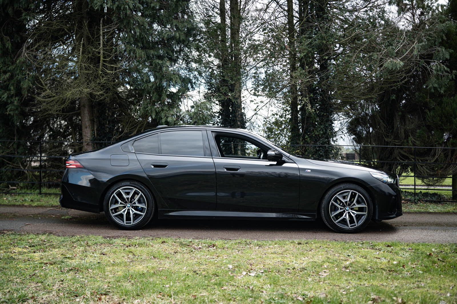 Black BMW 5 Series side profile on a country estate